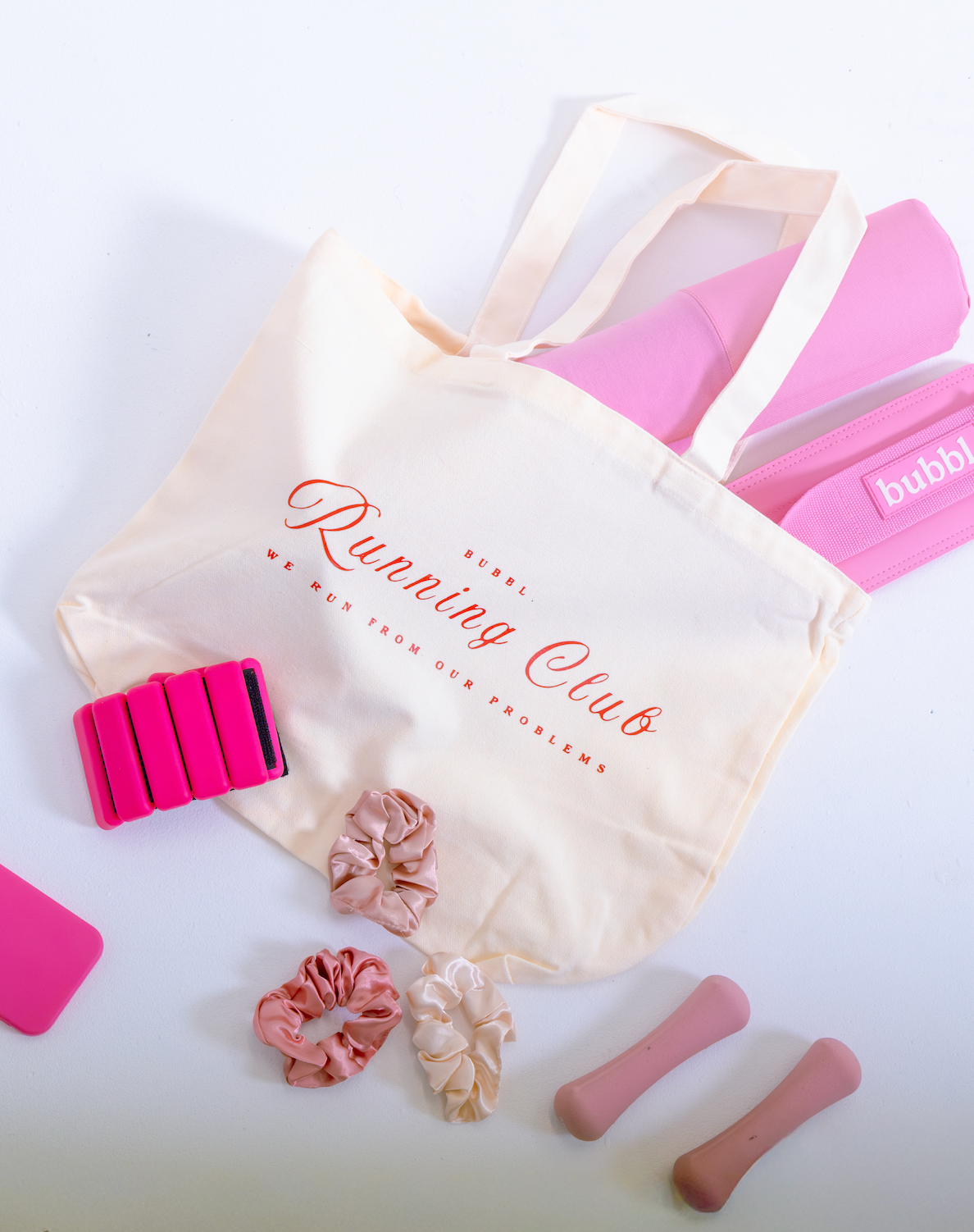 Bubbl. Running Club canvas tote bag with pink resistance bands and accessories laid flat on a white background
